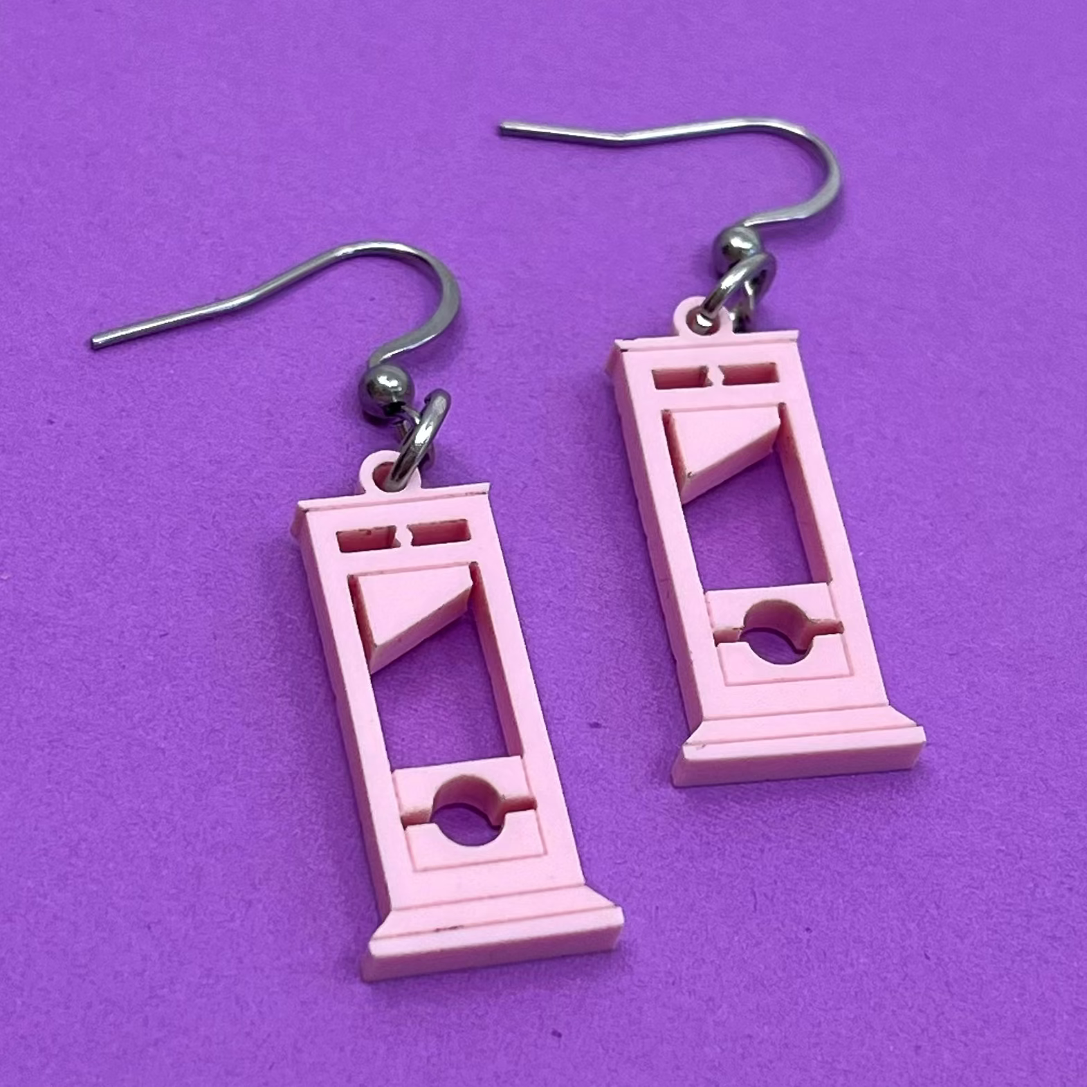 Pink guillotine-shaped earrings on a purple background
